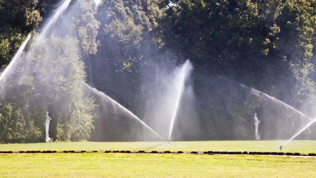 Gramado residencial com aspersores de irrigação jorrando água por cima do gramado.